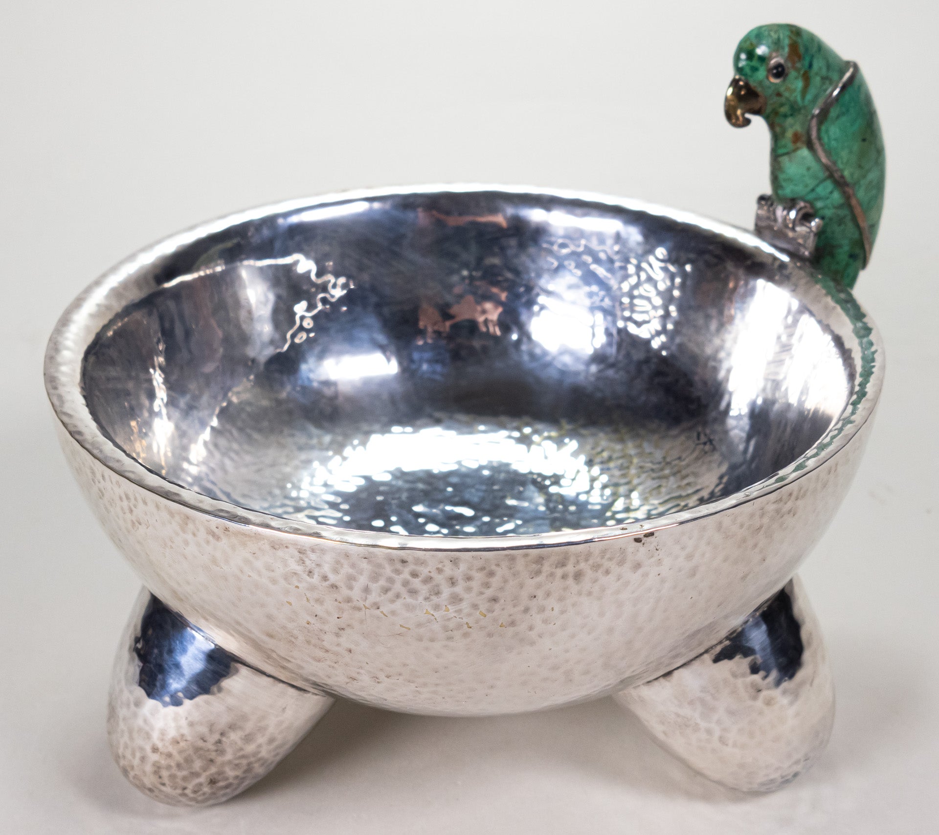 A silver-plated molcajete bowl with a malachite gem figure in the shape of a parrot.