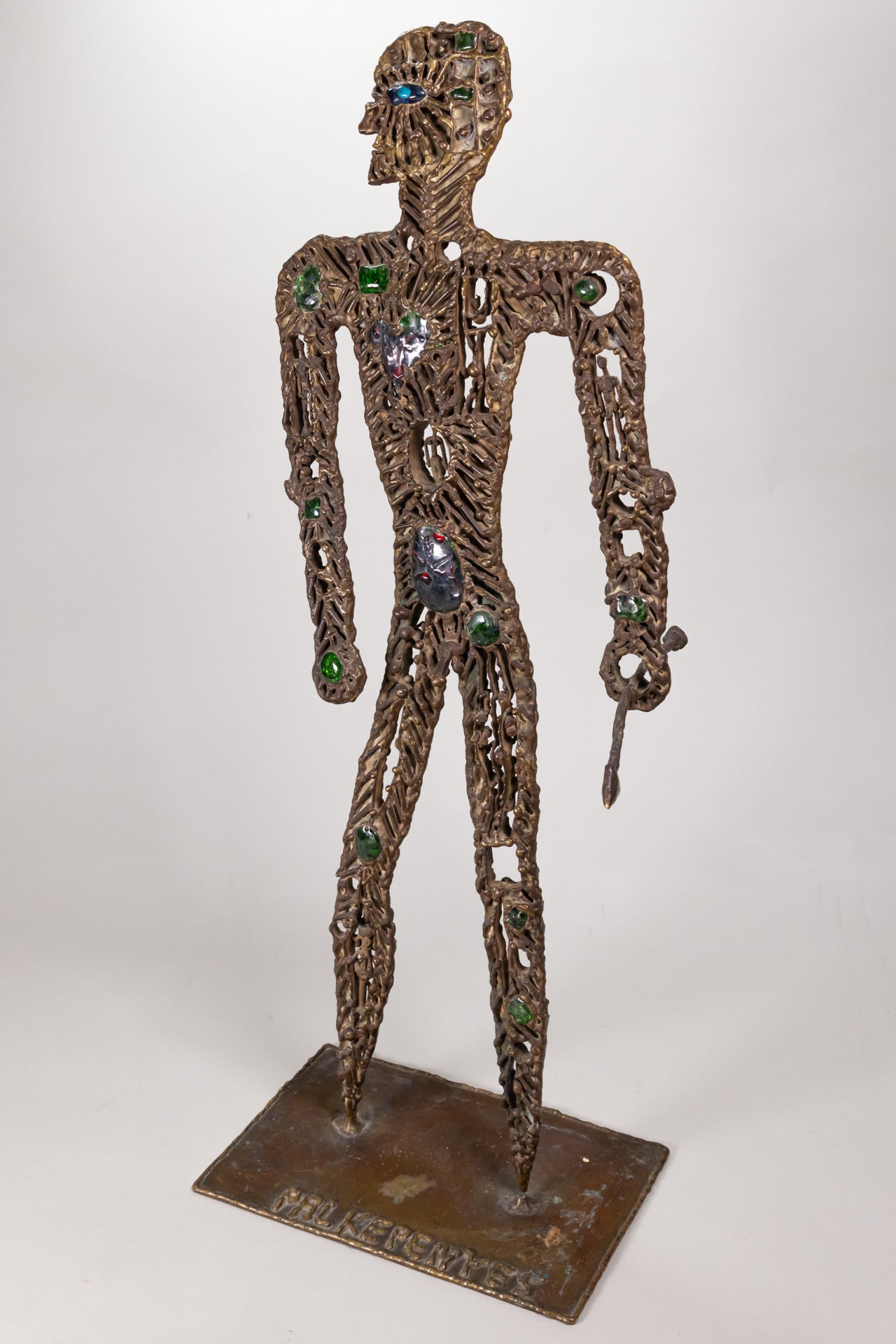 A brass metal sculpture of a hunter with gemstones and tiny figures ornate on it's body, holding a spear.