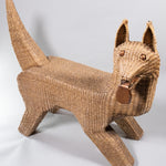 A seagrass woven over wire piece in the shape of a dog, looking to it's side with metal tongue hanging out.