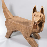 A seagrass woven over wire piece in the shape of a dog, looking to it's side with metal tongue hanging out.