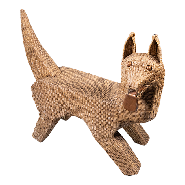A seagrass woven over wire piece in the shape of a dog, looking to it's side with metal tongue hanging out.