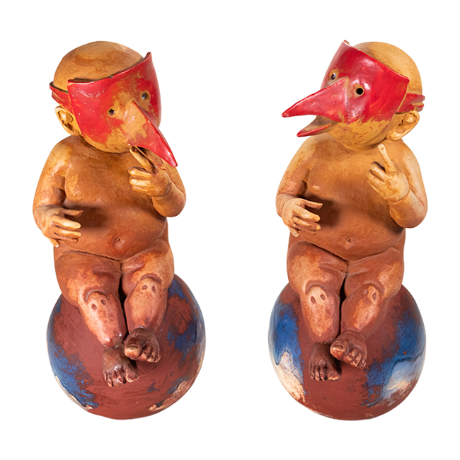A pair of matching ceramic pieces of chubby babies wearing red masks with long beaks, both sitting on orbs.