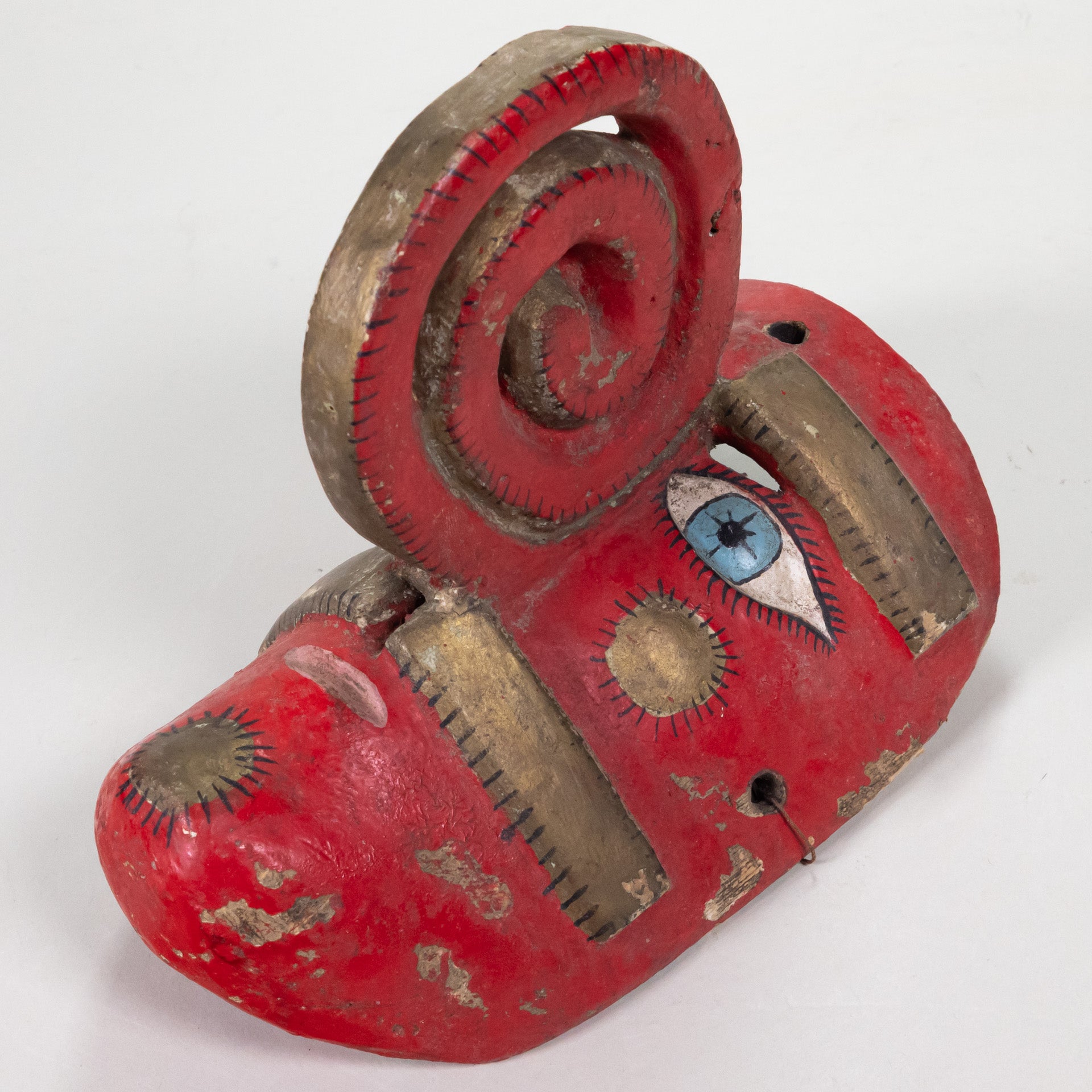 A red polychromed painted Nahua mask with a spiral nose and gold leaf painted details.