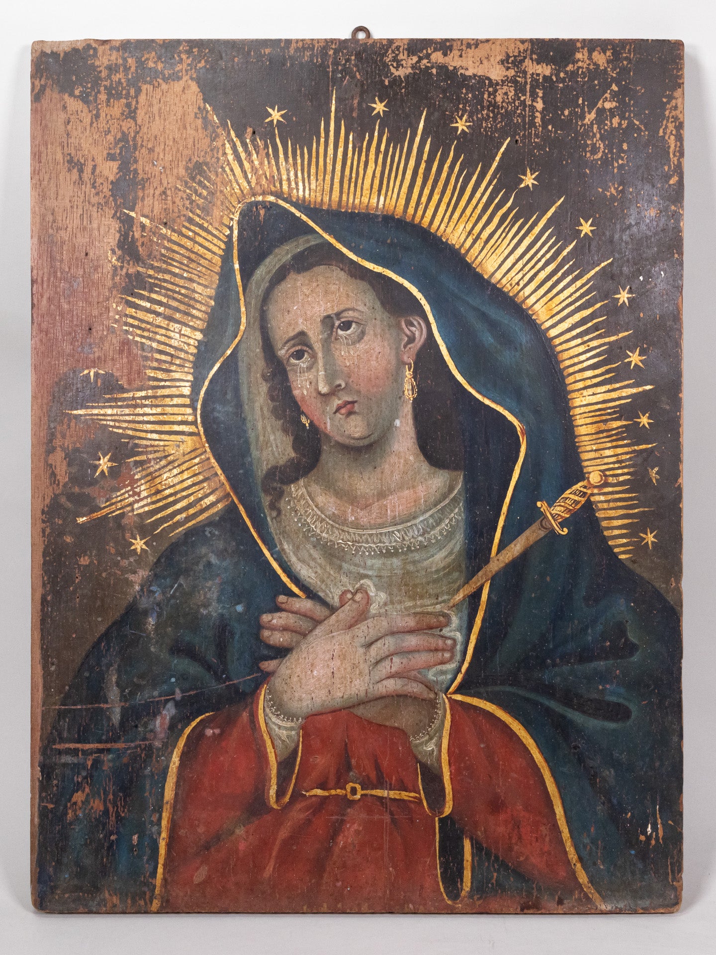Retablo painting of the Virgin Mary, grieving as tears fall from her eyes, hands clasp with a dagger piercing her heart.