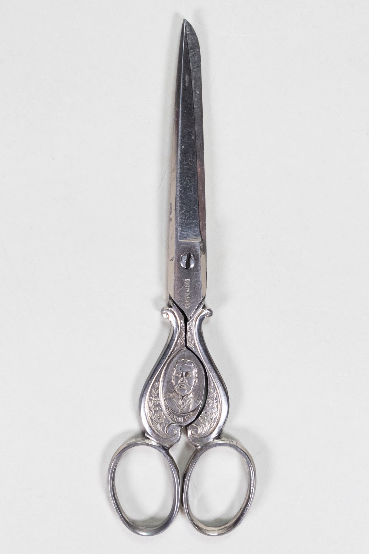 Silver sewing scissors decorated with a plant and floral design, with President Porfirio Diaz's bust.