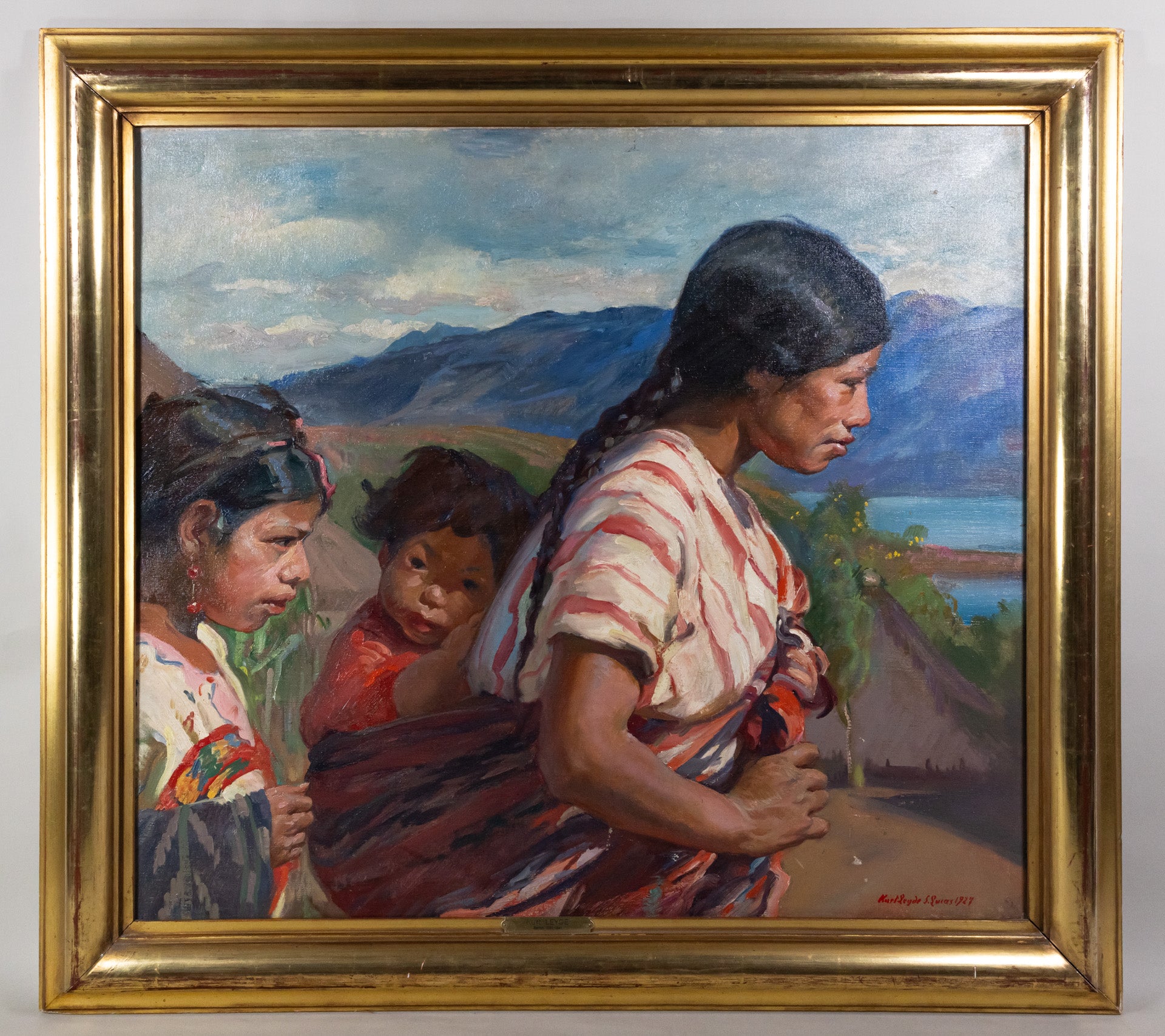Framed oil painting of an indigenous mother carrying her youngest child on a sling from her back, and her eldest daughter walking alongside them, with mountains and a body of water in the background.