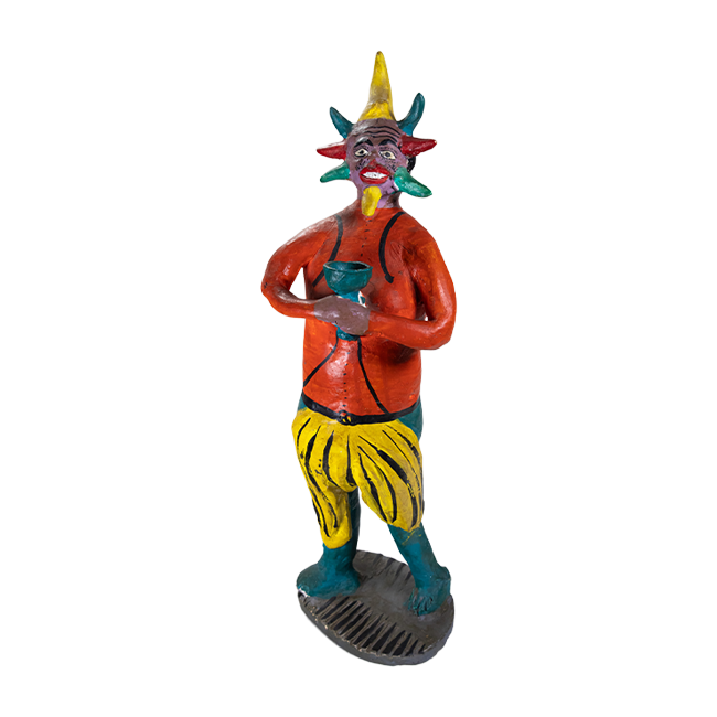 A tall ceramic sculpture of a devil holding a green cup and colorful horns around his face, and wearing an orange shirt with yellow and green bottoms.