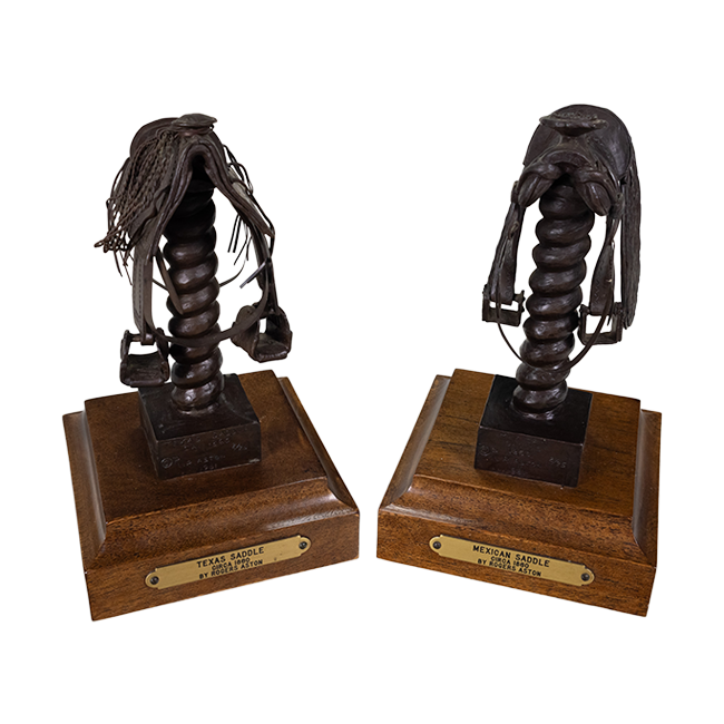 Two metal bronze saddles, one Texan and one Mexican, on wooden bases.