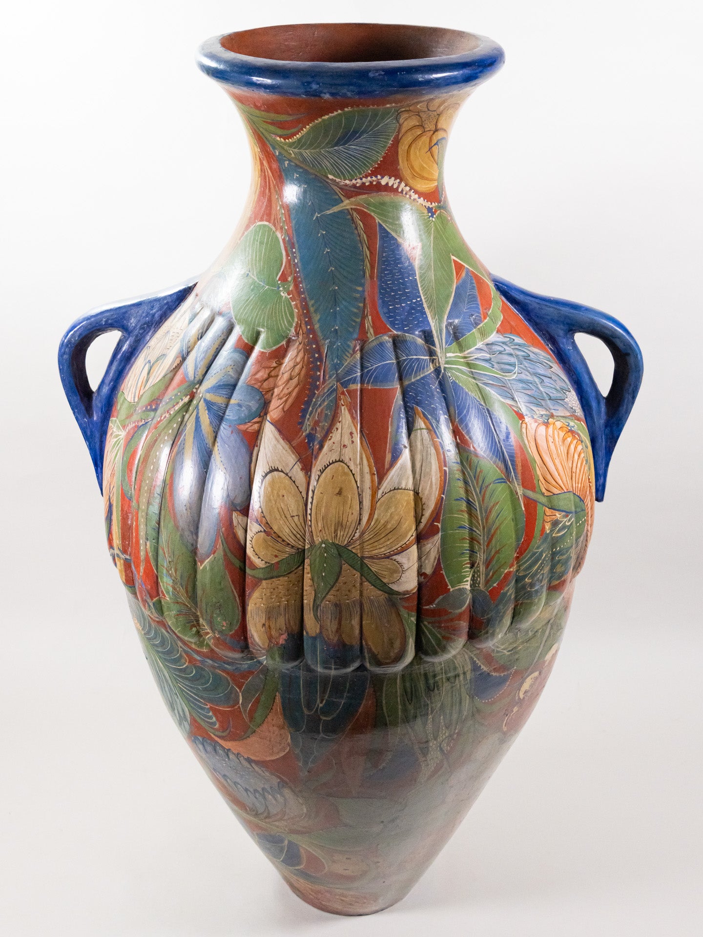 Large pottery vase with two blue handles and a floral design over orange color.