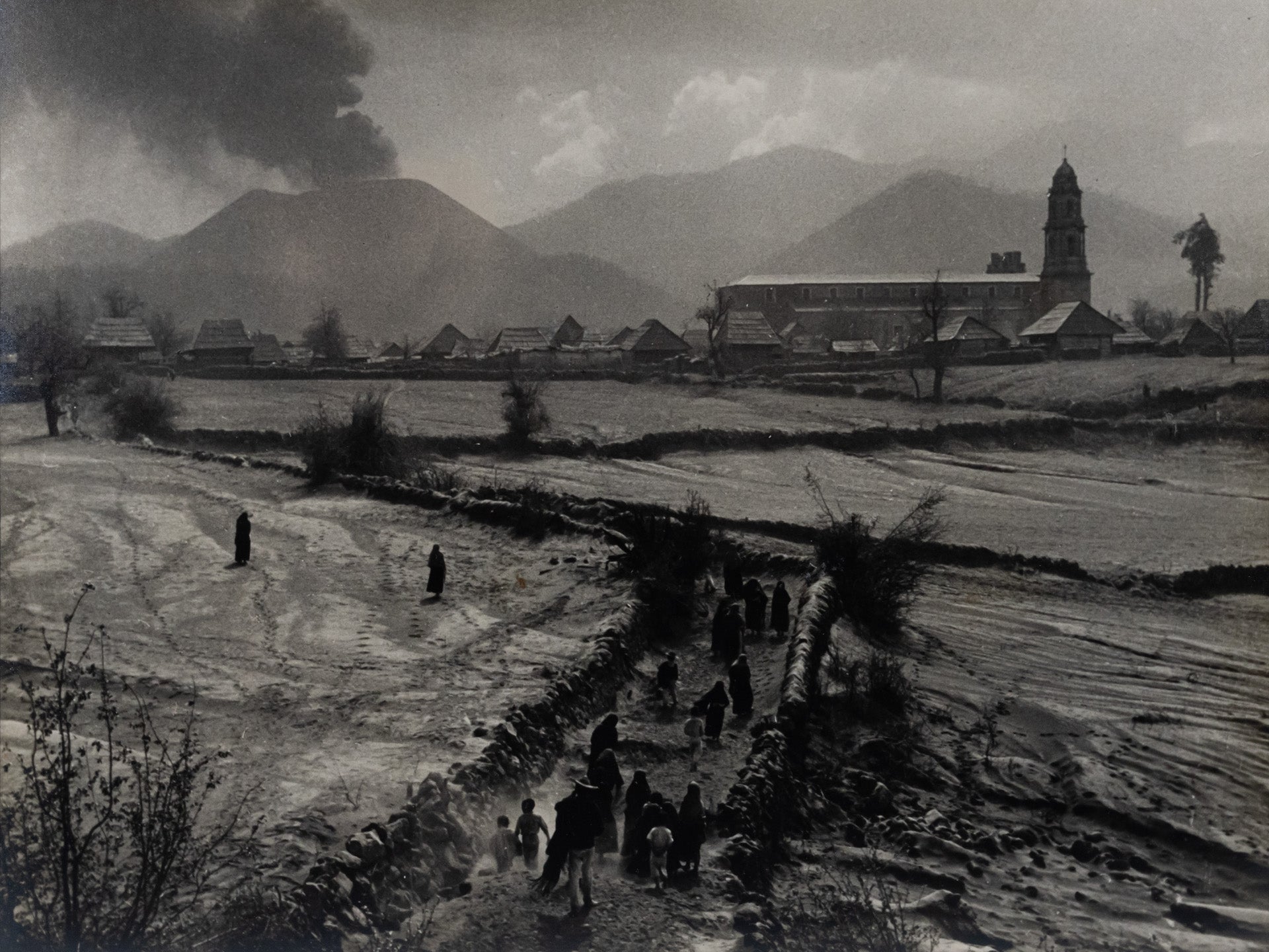 Black and white photograph of the Eruption of Parícutin with the Church of San Juan Parangaricutiro in the background.