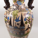 Large ceramic beige vase with crosshatches and brown handles, with elaborate artwork featuring church buildings, houses, villagers and animals.