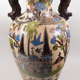Large ceramic beige vase with crosshatches and brown handles, with elaborate artwork featuring church buildings, houses, villagers and animals.